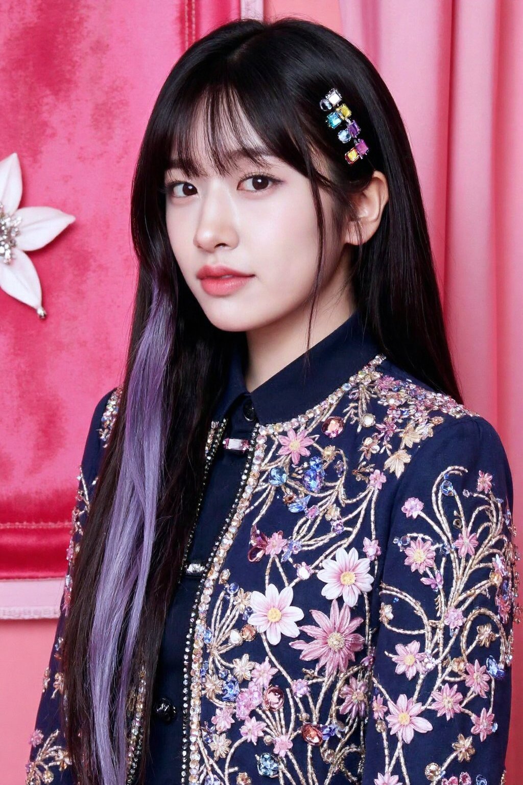 The image shows a young korean woman posing confidently against a luxurious pink velvet backdrop. She has long, straight hair with shades of black and lavender, adding a unique, stylish flair to her appearance. She is wearing an embellished jacket decorated with intricate patterns of gemstones, floral embroidery, and other ornamental details, giving her a regal and sophisticated look. Her makeup is soft yet striking, with bold eyeliner and a focus on her lips. Hair clips with colorful gems adorn her hair, adding to the overall glamorous vibe of the image.,  <lora:flux_realism_lora:1>,  <lora:makinaflux_ahnyujin_v1.0:1>