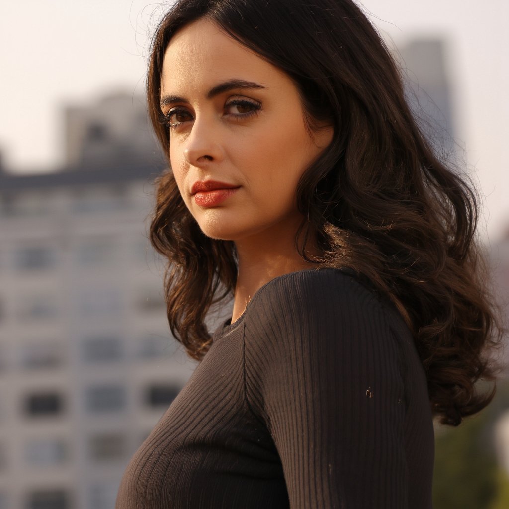 A portrait of krysten_ritter with long, wavy brown hair, captured in a side profile. She wears a black, ribbed top and her gaze is directed slightly to the side. Soft, warm lighting illuminates her face, highlighting her eyes and lips. The background is blurred, emphasizing the subject. The image conveys a serene and contemplative mood.