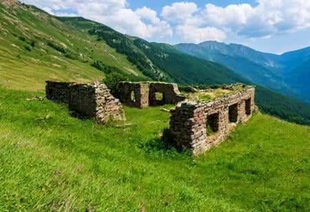 a grassy mountainous landscape in the summer, there are ruins visible in the distance. raw, photo, realistic