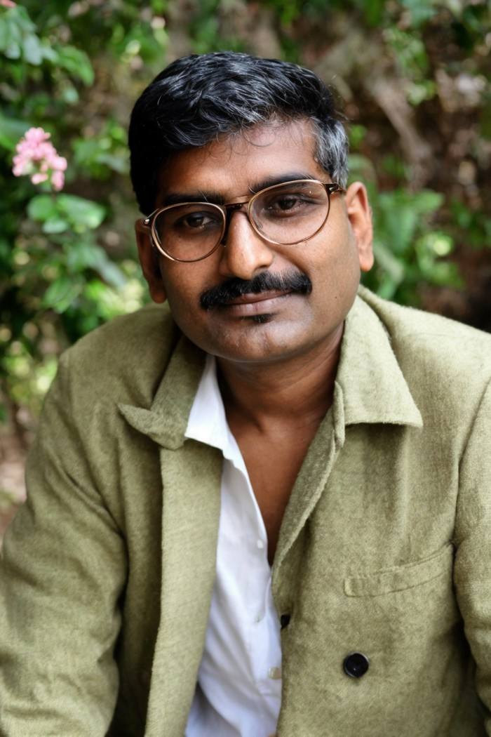 photo of a man, Indian, round glasses, thin eyebrows, writer