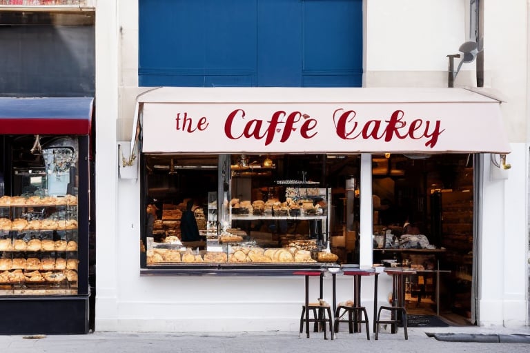 Looking down the street from viewpoint,  look the main objects,  from the street through the domestic-local bakery-cafe in Paris,  with a perfectly clean shop window,  in which there are,  fresh detailed bakery products,  two perfectly detailed chocolate cakes with whipped cream decorations,  on the awning of the bakery-cafe beautifully written letters,  detailed blue-red lettering of the bakery-cafe,  the awning is golden in color,  detailed and shimmers slightly in the gentle autumn sunlight,  under the large window of the bakery-cafe in perspective,  mathematically precise,  the wall in light cream color continues,  below is a horizontal ideal perspective,  a sidewalk,  with a realistic shadow from the building,  in the part of the shadow of the darker color of the sidewalk,  pebbles can be seen,  at the beginning of the bakery-café,  far away horizontally,  on the sidewalk,  a detailed board in the form of a pyramid,  with two sides,  light brown in color,  with a golden twisted sculpted top of the board along its length,  on blackboards,  clearly visible and legible,  written in white chalk,  the best bakery-café offers,  from croissants to coffee drinks,  several types,  with daily prices. In the bakery-cafe,  you can see through the window a chubby salesman with a mustache and a cap on his head,  black disheveled but neat hair,  a man of about 60 years old,  in a white shirt,  with an apron on,  in blue red yellow thin vertical stripes,  a little dirty from white of flour,  serves a customer,  a younger man in a beige suit,  with a classic hat in the same color tone,  a newspaper folded under his right hand,  while in his left hand he accepts a blue plate with a muffin perfectly covered with powdered sugar,  from the opposite side of the bakery-cafe,  a customer with a scarf around his neck in a white shirt and a gray suit vest,  drinking coffee from a sparkling clean cup,  and reading a newspaper on the counter in front of which he sits on a prochrome bar stool with a red leather round seat.