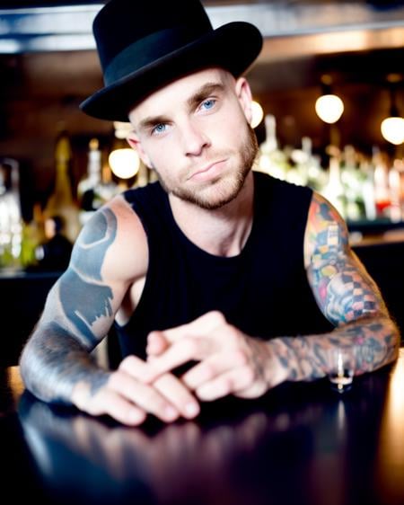 masterpiece realistic, best high quality, solo, arm tattoos, 1boy, black bowler hat, liquor bottles, reflection, looking at viewer, facial hair, shoulder tattoo, closed mouth, alcohol, indoors, short brown hair, upper body, blue eyes, bar (place), black tank top, lips, head resting on hands together, arm hair, backlighting, sfw