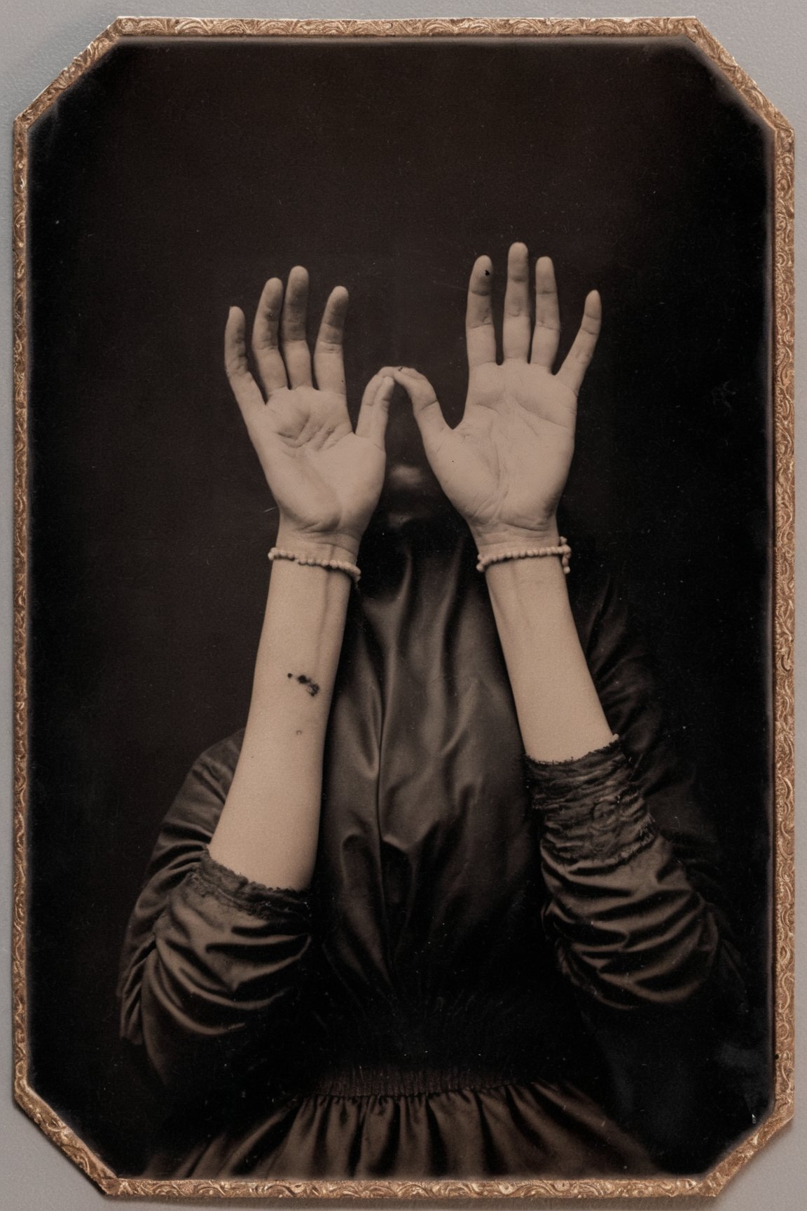 hyperrealistic tintype photo of a woman's hands, palms facing up, holding a small pile of sparking black sand, pale flawless skin, delicate details. extremely high-resolution details, photographic, realism pushed to extreme, fine texture, incredibly lifelike, ornate border, tintime <lora:timetravel_xl:1> 