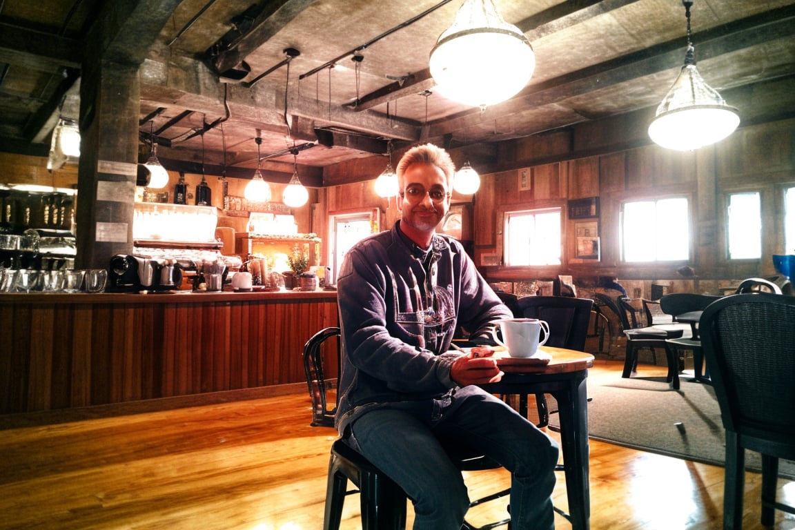 indoor coffee shop. DJ Lovin'U is sitting on a table with a coffe, looking at viewer, upper body shot, natural_background