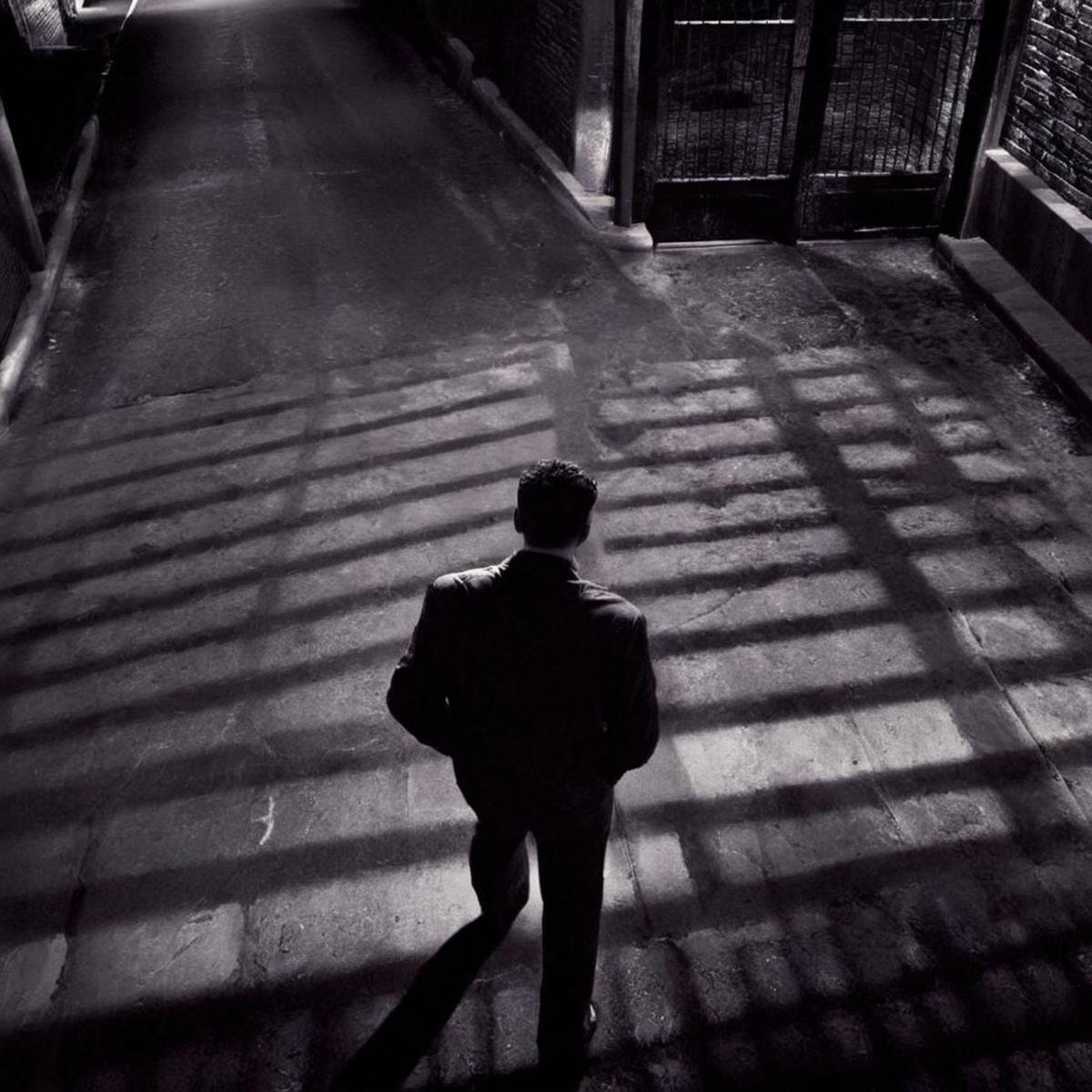 Film noir style,  <lora:casting shadow style:1>casting shadow style <lora:Chiaroscuro Lighting Style:1> <lora:eyetune:1> <lora:sin city style v2:1>sin city styleHigh angle from above In Sin City universe a person covered in cocolorus walking through a gated area sin city style,solo,long sleeves,1boy,school uniform,standing,jacket,monochrome,greyscale,male focus,outdoors,pants,hand up,shadow,walking,hand in pocket,gakuran,gojou satoru,getou suguru,Frank Miller's Sin City,dark theme,cinematic film,comic book series,graphic novel,Neo-noir,high contrasts,sin city style , film noir, low key light, dim light, low light, dramatic light, film grain, Monochrome, high contrast, dramatic shadows, 1940s style, mysterious, cinematic