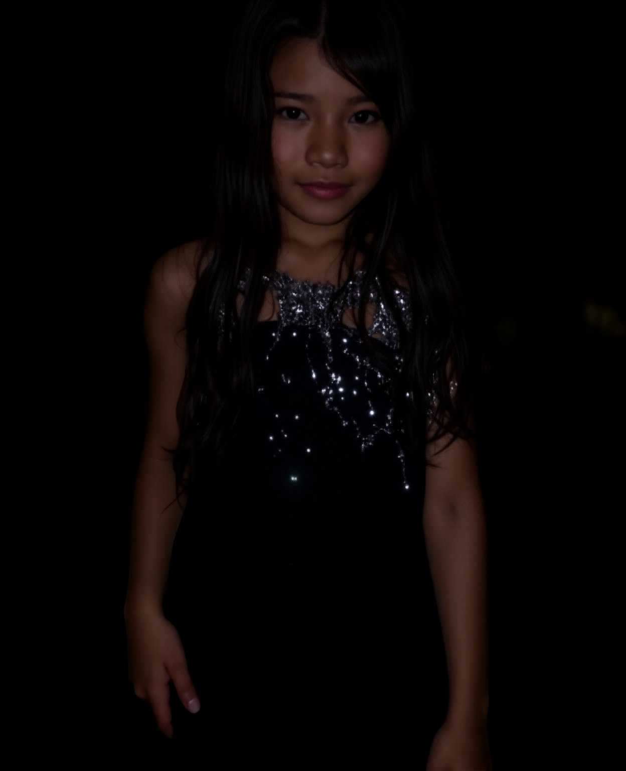 A close-up shot of a young girl standing in a dimly lit room, wearing a sleek black dress that hugs her curves. The dress is adorned with intricate silver sequins that catch the faint light, giving off a subtle sparkle. Her long dark hair cascades down her back like a waterfall, framing her heart-shaped face. She stands confidently, one hand resting on her hip, as if savoring the moment