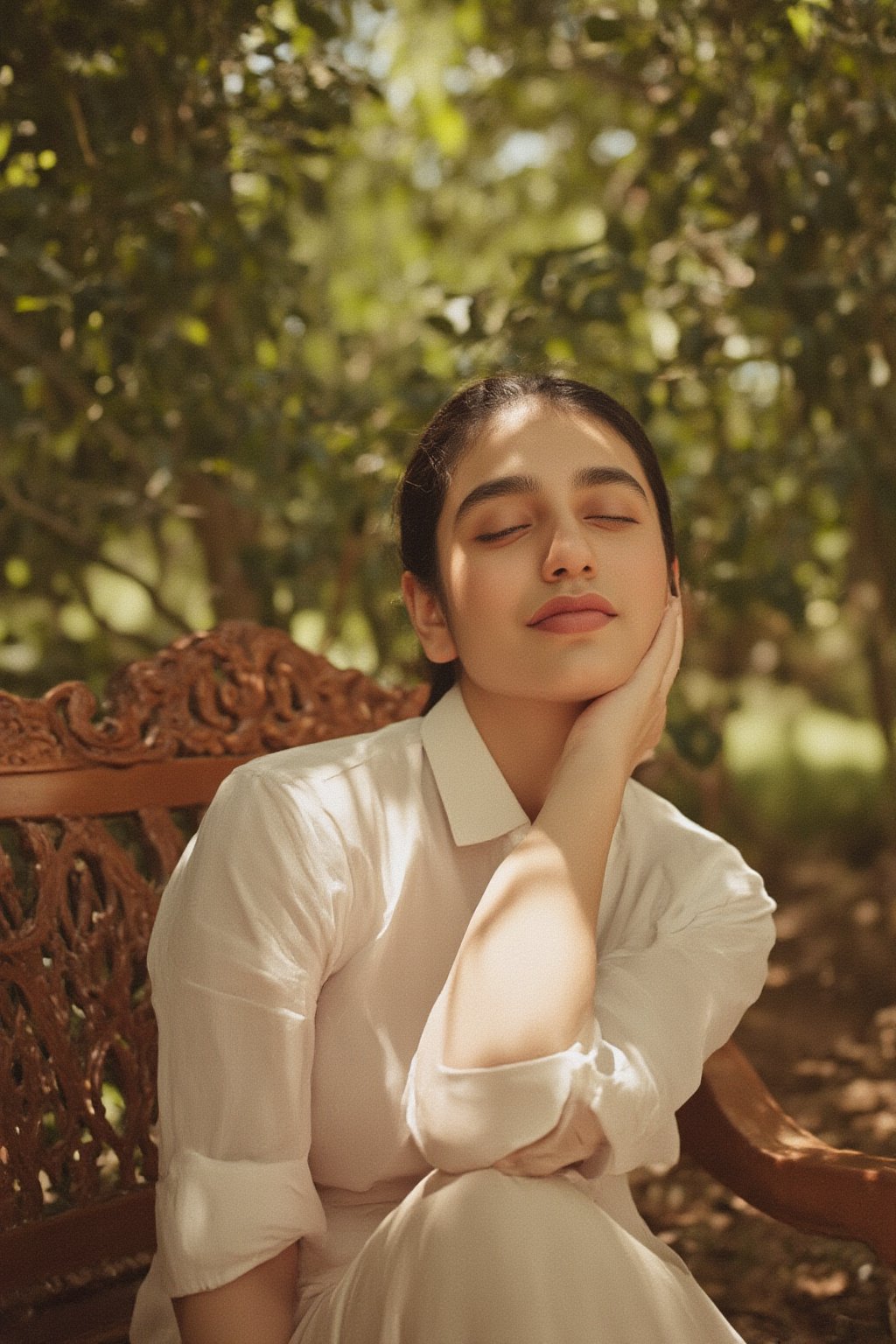 A warm sunlight illuminates Kalyani Priyadarshan's serene expression, set against a soft focus background of lush greenery. Her gentle smile and closed eyes evoke a sense of peace, as she sits cross-legged on a intricately carved wooden bench amidst the tranquil surroundings.