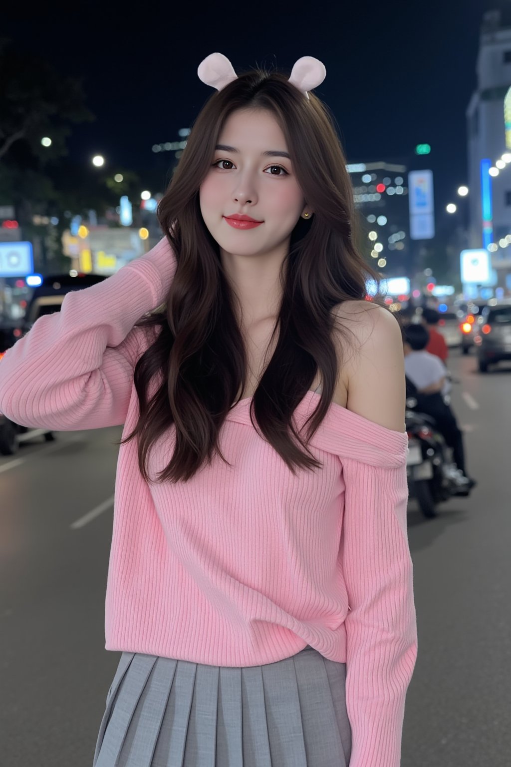 The image is a portrait of a young woman standing in front of a city skyline at night. She is wearing a pink off-the-shoulder sweater and a gray pleated skirt. Her long dark hair is styled in loose waves with white bunny ears and she is looking directly at the camera with a slight smile on her face. The background is blurred, but it appears to be a busy street with cars and motorcycles. The overall mood of the image is casual and relaxed.
