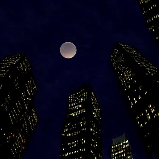 night, dark blue sky with blurry white clouds, full moon, black rectangular skyscrapers with small windows in which white light is visible, metal superstructures are visible at the tops of skyscrapers, brown cubes and a few gray cubes are visible at the base of skyscrapers, the earth is brown mud or clay,