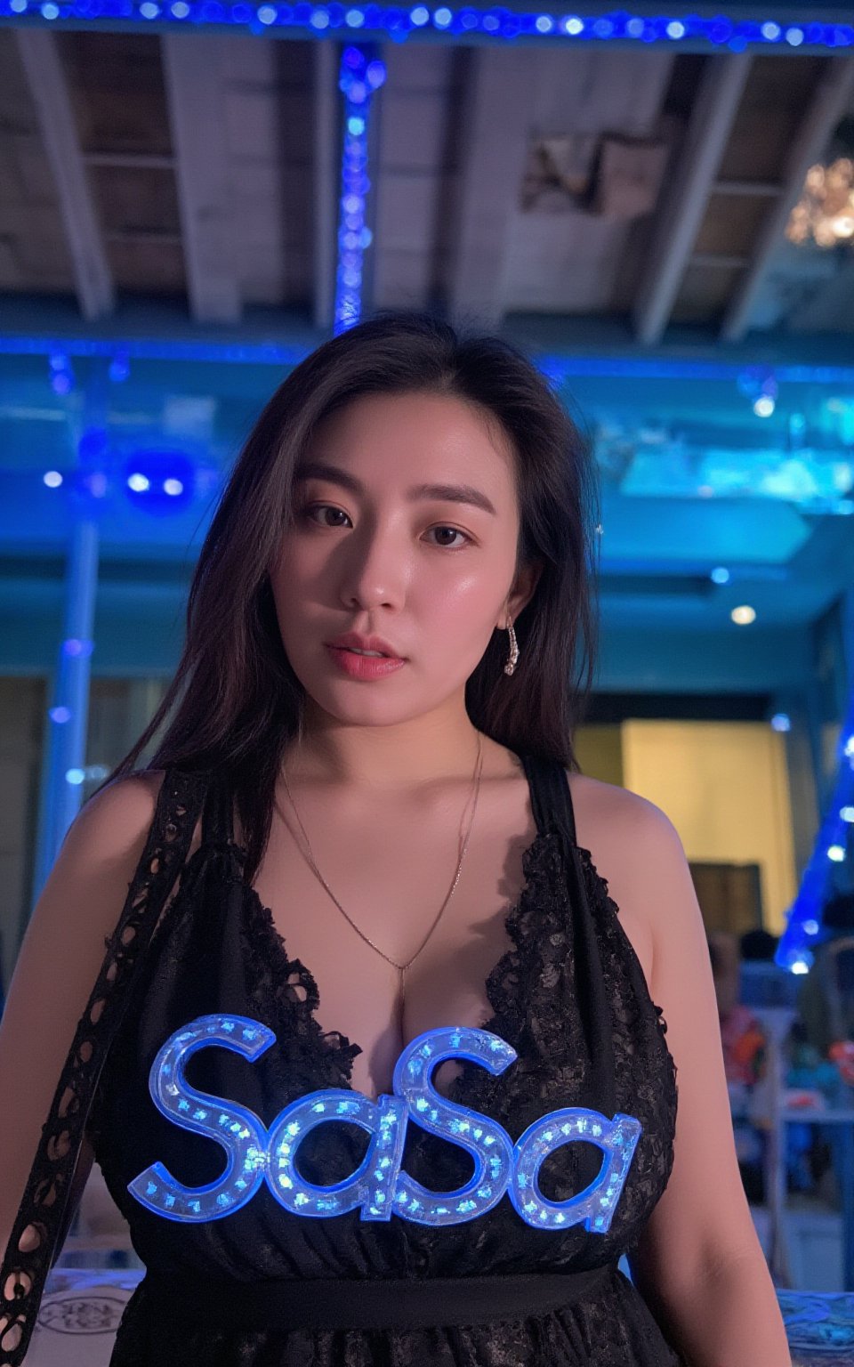 a hubgwoman with long dark hair, wearing a black lace dress, adorned with a necklace and earrings. The woman's chest is adorned with blue letters that spell out "SaSa" in a glowing light-up font. The backdrop is a vibrant blue, with a few colorful lights in the distance.