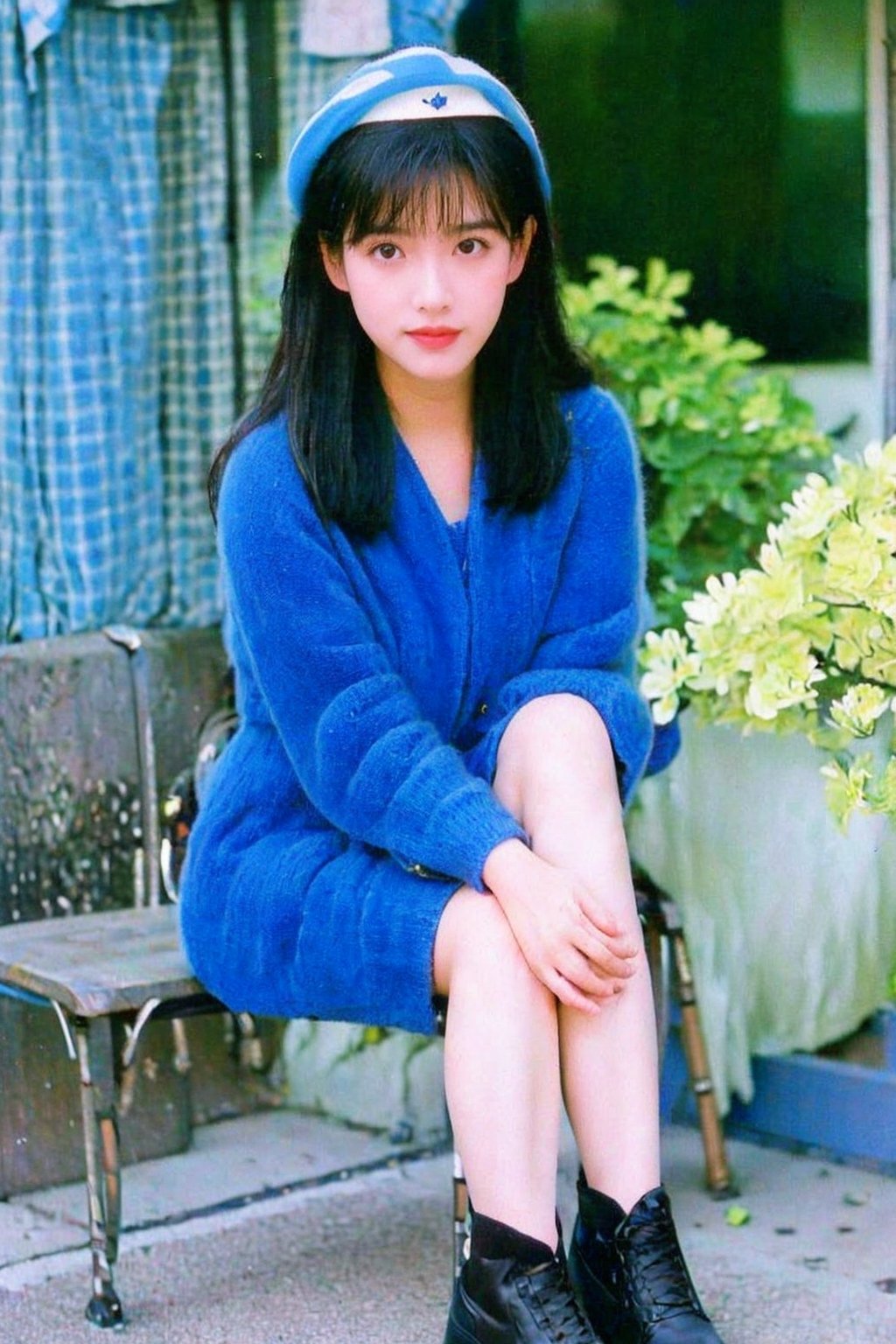 1girl, Vivian Chow2, solo, long hair, looking at viewer, bangs, black hair, long sleeves, full body, flower, outdoors, day, blunt bangs, mole, blurry, black eyes, hong kong high school uniform, white sock, black leather shoe, blue school dress, big breasts, blurry background, white headwear, sitting on a bench, in front of school, photo background, hongkong 80s,Vivian Chow2, HKgirl2,realhands