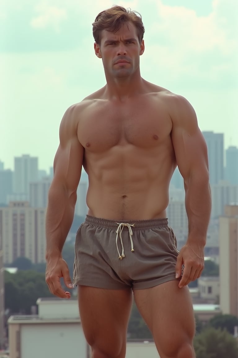 A full-length photograph of a mid-30s man in the 1970s. He is wearing short athletic shorts and no shirt. His beefy, well-worked body stands out. Hair on his armpits, legs, chest and arms. The city can be seen in the background.