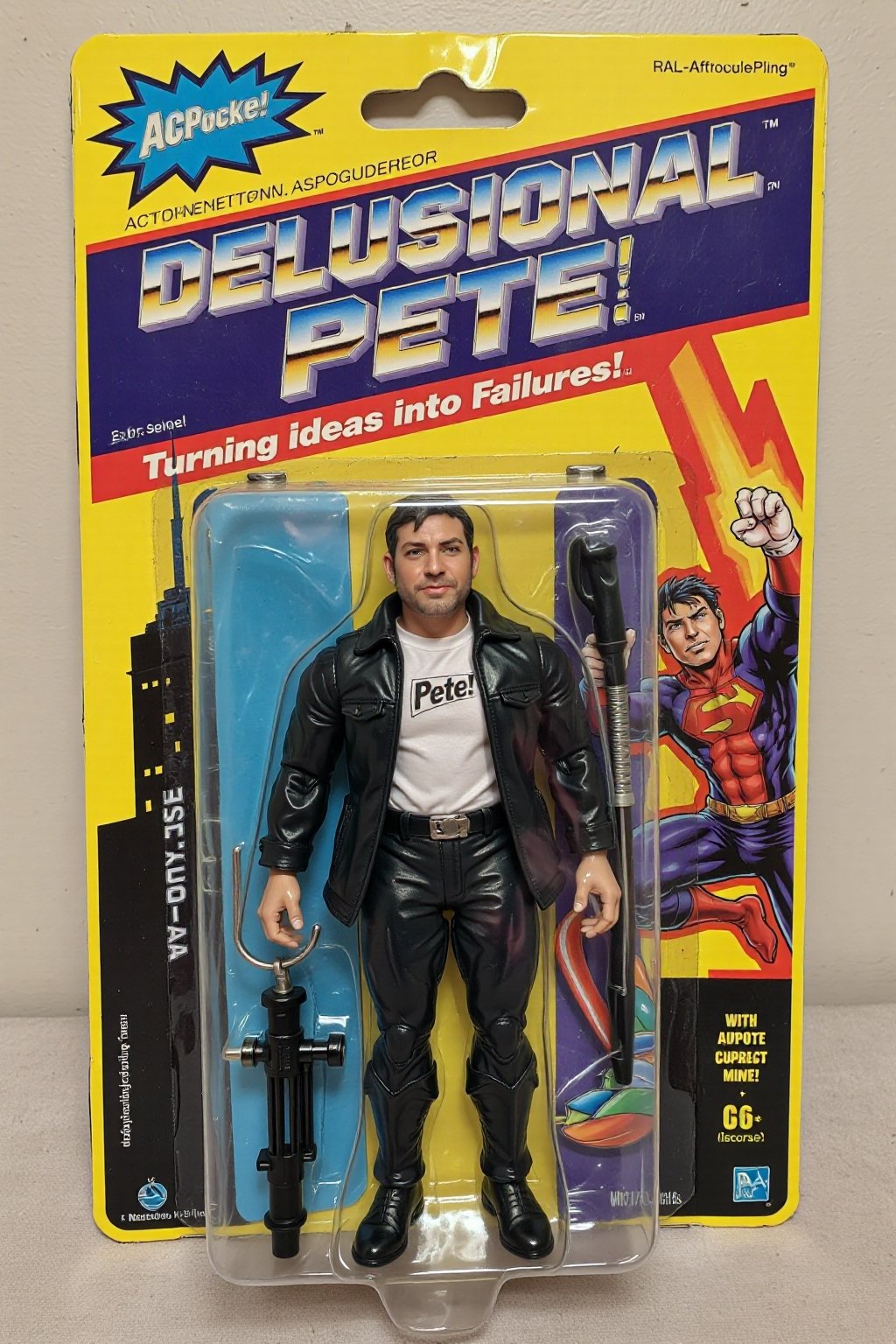 An unopened action figure package featuring "Delusional Pete" a superhero (psmoguel) who has the power to turn ideas on failures. The action figure stands proudly in the package, wearing a black jacket and white shirt with the word "Pete" on his chest. The packaging is colorful and bold, with comic-style illustrations of "Delusional Pete" in action on the sides. The name "Delusional Pete" is written in big, bold, metallic letters at the top, with the tagline "Turning ideas into failures!" above. The background inside the package is a cityscape, reinforcing the superhero theme with a ral-afpacking logo at the top-left corner. 