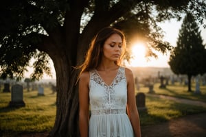 Photo. Profile of a woman in a lace summer dress. She is standing beside a tree with her eyes closed, facing the morning sun. The background is a cemetery.