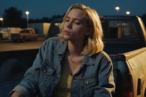 Closeup of a blonde young woman smoking a cigarette sitting on the back of a dusty pickup truck in a dimly lit parking lot at night. She is holding the cigarette with her hand. Her outfit consists of a denim jacket. The truck's tailgate is down, revealing a jumble of boxes and crates. The atmosphere is moody and mysterious, with the yellow glow of the streetlight casting long shadows and reflecting off the truck's metal surface.