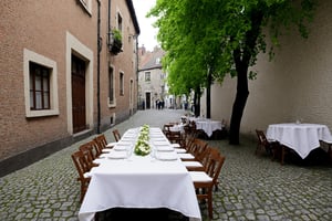 a table with a white tablecloth is set up outside on a cobblestone street.
