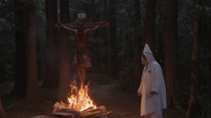 cinematic close-up vintage shot film still, a cinematic motion picture film, artistic creative color photography style, Kodak color film style, cinemascope, film grain, real creepy horror scene, (an old man in white Ku Klux Klan clothes with a long hood stands near a burning crucifixion cross to which a black man is tied. location of an evening forest glade.) 1980s horror.