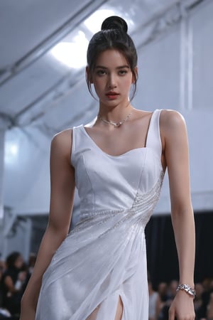 a model walks down a runway in a white sleeveless dress. The dress is adorned with a sheer neckline and a low cut skirt. Her hair is pulled back in a ponytail, adding a touch of texture to her face. The backdrop is a stark black, creating a stark contrast to the model's white dress. To the left of the model, another model's legs can be seen in the lower left corner of the frame, adding depth to the composition.