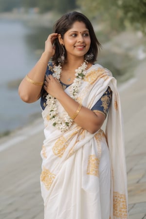 a woman dressed in a white saree adorned with gold bands and a gold necklace. She is adorned with a gold ring, earrings, and a garland of white flowers. Her hair is styled in a sleek bob, and she is smiling. The saree is draped over her left shoulder, adding a touch of contrast to her outfit. The backdrop is blurred, suggesting a natural setting.,Payal,Mallu beauty 