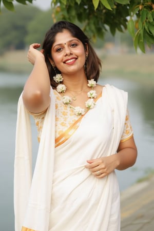 a woman dressed in a white saree adorned with gold bands and a gold necklace. She is adorned with a gold ring, earrings, and a garland of white flowers. Her hair is styled in a sleek bob, and she is smiling. The saree is draped over her left shoulder, adding a touch of contrast to her outfit. The backdrop is blurred, suggesting a natural setting.,Payal,Mallu beauty 