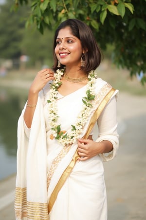 a woman dressed in a white saree adorned with gold bands and a gold necklace. She is adorned with a gold ring, earrings, and a garland of white flowers. Her hair is styled in a sleek bob, and she is smiling. The saree is draped over her left shoulder, adding a touch of contrast to her outfit. The backdrop is blurred, suggesting a natural setting.,Payal,Mallu beauty 