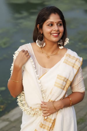 a woman dressed in a white saree adorned with gold bands and a gold necklace. She is adorned with a gold ring, earrings, and a garland of white flowers. Her hair is styled in a sleek bob, and she is smiling. The saree is draped over her left shoulder, adding a touch of contrast to her outfit. The backdrop is blurred, suggesting a natural setting.,Payal,Mallu beauty 