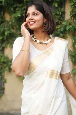 a woman dressed in a white saree adorned with gold bands and a gold necklace. She is adorned with a gold ring, earrings, and a garland of white flowers. Her hair is styled in a sleek bob, and she is smiling. The saree is draped over her left shoulder, adding a touch of contrast to her outfit. The backdrop is blurred, suggesting a natural setting.,Payal,Mallu beauty 