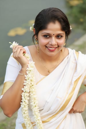 a woman dressed in a white saree adorned with gold bands and a gold necklace. She is adorned with a gold ring, earrings, and a garland of white flowers. Her hair is styled in a sleek bob, and she is smiling. The saree is draped over her left shoulder, adding a touch of contrast to her outfit. The backdrop is blurred, suggesting a natural setting.,Payal,Mallu beauty 