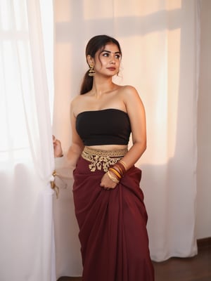 a medium-sized sexy indian woman stands in sidewise in front of a white curtain. She is dressed in a black sleeveless blouse with a maroon sari adorned with gold embroidery. Her hair is pulled back in a ponytail, and she is adorned with a pair of dangling earrings. Her bangles are gold, adding a touch of contrast to her dress. The backdrop is a stark white, creating a stark contrast to the woman's outfit.,photorealistic,Anupama, Warm Lighting,TamannaFlux, IMG0095.HEICl Viewing at camera in a  sensual way,Gil25yo,Futuristic 