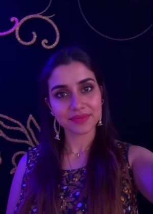 a beautiful  woman stands in front of a dark backdrop, adorned with a gold necklace and earrings. She is dressed in a sleeveless black dress with a brown and gold pattern. Her hair is long and cascades down to her shoulders, framing her face. The backdrop is adorned with gold swirling designs, adding a touch of luxury to the scene. The lighting is subdued, creating a stark contrast to the dark backdrop.,Sahana15 