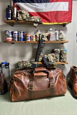 A rustic survival bunker wall in a southern US setting, adorned with an assortment of firearms, ammunition, and emergency supplies. The concrete walls are lined with shelves, stacked high with canned goods, water bottles, and MREs. A southern states flag hangs proudly above the entrance, surrounded by camouflage gear and hunting equipment. In the foreground, a pair of rugged boots and a holstered pistol sit atop a worn leather duffel bag.