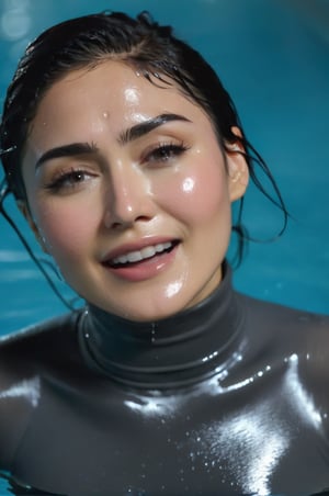 Daniella Pineda, emerging from the water. Her head and shoulders are visible above the surface of water. She looks surprised but laughing, her dark grey turtleneck top wet and clinging to her, with water droplets sparkling around her. She is in the middle of an indoor pool and splashes from her emergence, fully drenched, dripping wet, wet hair, face wet, face drenched