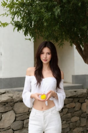 a woman with long dark brown hair, wearing a white off-the-shoulder, long-sleeved shirt and a pair of white pants, is stunning. She is holding a small, round, yellow object in her hands, adding a pop of color to her outfit. The backdrop, a stone wall, and a tree with green leaves, adds a touch of greenery to the scene. A white building can be seen in the background.