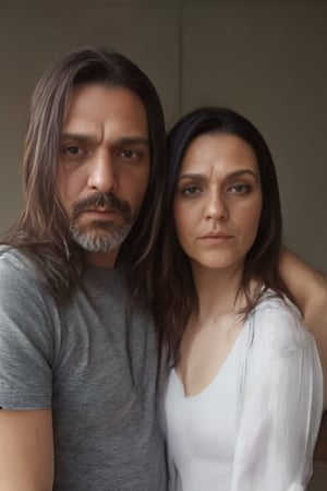 Gasty stands tall on the left, his grey t-shirt and jeans a casual contrast to Paola's crisp white top and brown boots on the right. Both gaze directly at the viewer, their features illuminated by soft, natural light. Gasty's long, brown locks cascade down his back, while Paola's straight black hair falls like a curtain along her shoulders, framing their profiles against a subtle background.