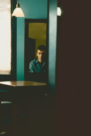 A grainy reflection in an old mirror, showing a person with a solemn expression looking at a camera in their hand, in a dimly lit room, with a film grain effect, in the style of Edward Hopper