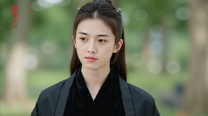 The image is a close-up portrait of a young Asian woman with long dark hair tied up in a high bun. She is wearing a black traditional Chinese outfit with a black shawl draped over her shoulders. The woman is looking directly at the camera with a serious expression on her face. The background is blurred, but it appears to be a park or garden with trees and greenery. On the right side of the image, there is a logo with Chinese characters written in red., cfairy