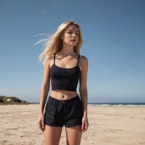 A young woman with long blonde hair stands confidently on the beach, her gaze directed towards the horizon. Her black crop top and black shorts contrast sharply with the sandy beach and clear blue sky. The image is taken from a low angle, emphasizing her height and stature, and it's bathed in natural light, highlighting the textures of the sand and the fabric of her clothing. The overall composition of the image suggests a sense of freedom and tranquility.