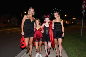 A gorgeous photo of a mother and her two  tween daughters, dressed in sexy Halloween costumes, holding a candy bag, walking on the footpath of a quiet suburban Australian street at night, trick or treaters, Halloween theme, smiling for the camera