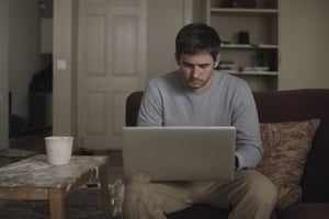Sad man working at a laptop alone in a dirty living room
