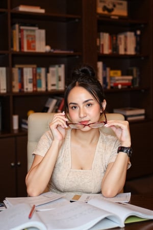 A woman sits at a desk, gazing directly at the camera. She wears a creambeige lace top, paired with large hoop earrings and a sleek black watch on her left wrist. Her dark hair is styled in a neat hairdo. With her right hand, she holds a pair of red glasses up to her face, while her left hand grasps a pencil. Papers are scattered across the desk before her. The background features a sturdy dark wood bookshelf lined with volumes, creating a warm, scholarly atmosphere. bokeh, depth of field