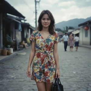 Captured at eye-level on a cloudy day, a young Asian woman stands on a cobblestone street, her shaggy wolf cut hair cascading over her shoulders. She is wearing a short-sleeved, multi-colored dress adorned with a floral pattern. Her dress is tied at the waist, adding a pop of color to the scene. The woman's dress is adorned in a variety of colors, including red, yellow, green, and blue. She's holding a black bag in her left hand, and her right hand is resting on her hip. The backdrop is blurred, with a mountain range in the distance. To the right of the woman, a man and a woman can be seen walking down the street.,Dyn4Kay,Analoquer