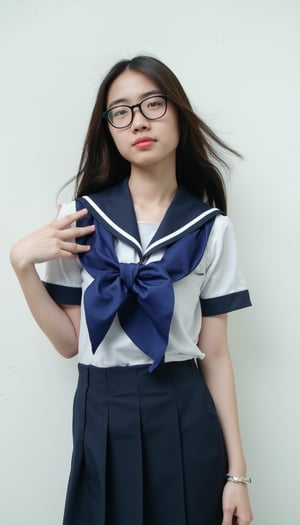 a young woman, dressed in a navy blue and white school uniform, adorned with a blue scarf tied around her neck. She is standing in front of a white wall, her hair cascading over her shoulders, adding a touch of movement to her face. She's wearing a pair of black framed eye glasses, her left hand resting on her hip. Her right hand is draped over her right shoulder, adding depth to the composition.