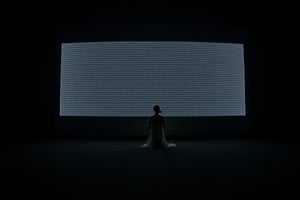 A dramatic photograph of a woman kneeling in prayer before a massive, wall-sized TV screen displaying static noise. The woman is positioned in the center of the frame, her hands clasped in front of her, head bowed in deep reverence. She is wearing a simple, long flowing dress, with her hair loosely tied back. The room around her is dark and minimalistic, illuminated only by the flickering light from the static on the TV screen, casting sharp shadows. The scene has a somber, contemplative mood, emphasizing a sense of devotion amidst technology. Cinematic lighting, high contrast, wide-angle shot, surreal atmosphere, dystopian vibe.

The room around her is stark and minimalist, with the gigantic TV as the focal point. The screen itself is a monolithic presence, slightly curved, and its glossy frame gleams faintly in the low ambient light. The static, constantly moving, seems alive, with random flashes and bands of light darting across the screen, filling the atmosphere with a sense of both unease and wonder.

The visual style blends realism with an unsettling, surreal tone, evoking themes of dystopian futurism. The lighting is harsh yet intimate, with sharp contrasts between the illuminated woman and the darkened surroundings. The static creates a grainy, almost tactile texture against the smooth surface of the TV, while the woman's posture exudes a sense of quiet devotion, creating a powerful juxtaposition between the spiritual and the technological. The overall composition is cinematic, like a still frame from a futuristic, introspective narrative, where technology looms as a vast, enigmatic presence.
