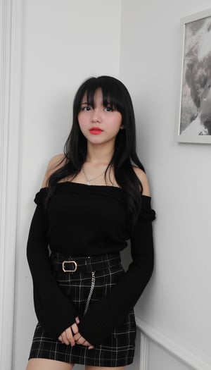 A young Asian woman stands confidently in front of a crisp white wall, dressed in a striking ensemble. Her long, dark hair cascades down her back as she wears a black off-the-shoulder shirt with long sleeves, paired with a plaid black skirt and matching belt featuring a gold buckle. A pop of vibrant red color accentuates her lips, drawing attention to her facial features. Around her neck, a silver chain adorns the necklace that catches the light. To her right, a framed black and white photograph of a woman's face adds an intriguing element to the scene, creating a sense of depth and visual interest.