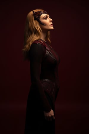 Professional studio photography. A woman dressed in a dark, fitted suit with details in red and black tones. The woman has long, wavy blonde hair and wears a crown on her head. She stands in front of a dark red backdrop, looking up with a calm expression. Side portrait, profile, dramatic close-up, dramatic lighting, ray tracing