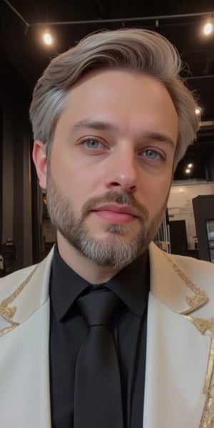 An animated portrait of a young man with light gray short beard and hair and blueish green eyes. He is wearing a black collared shirt with a black tie and a white jacket with gold trim. The jacket has two gold buttons on the front of it. Behind him is a black ceiling with lights on it.