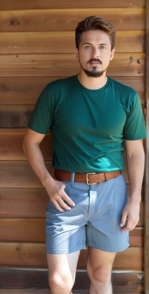 Captured at eye-level, a medium-sized man stands on a wooden deck in front of a wooden wall. He is dressed in a short-sleeved green t-shirt, brown shorts, brown shoes, and a brown belt. His left hand is holding a blue and white hat, while his right hand is resting on his hip. His hair is short and dark, and he has a goatee and mustache. His eyes are squinted. The sun is shining on the left side of the image, casting a shadow on the wooden deck.