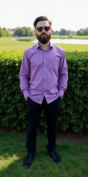 a man stands in front of a hedge, dressed in a purple button-down long-sleeved button-up shirt, black pants, and black shoes. He has a short brown beard, mustache, and brown sunglasses on his face. His hair is neatly combed, and he is standing in a field of grass, with a body of water in the background. The sky is a pale blue, and the sun casts a shadow on the grass.