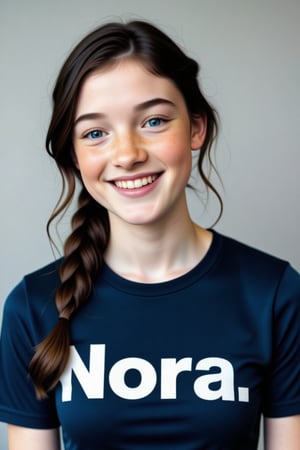 close-up portrait shot of an 30 year old woman wearing a dark blue teeshirt with the word "Nora." emblazoned on it in bold white block text, laughing and smiling, gazing into the camera lens at an angle. The subject's black hair is long and in a plait, framing her pale eavily freckled Irish face against a clean and minimalist background. The overall focus is on the subject's facial features.,