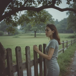 Film_19, A young woman stands serenely beside a weathered wooden fence, a slightly pensive yet hopeful expression on her face, under a leafy tree on a slightly overcast day. [Photography, photorealistic, reminiscent of 1950s/60s snapshot], [No specific artist reference, aiming for a candid, documentary style], [Shallow depth of field, focusing on the woman, slightly grainy film texture, muted natural light with slightly cool tones, Kodachrome-like color palette, background slightly blurred with a focus on the fence and tree, wet grass visible, natural setting, slightly desaturated colors for a vintage feel. Virtual19